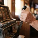 A player's hand calmly pulls the worn lever of a classic mechanical slot machine, seen in a close-up from a slight low angle